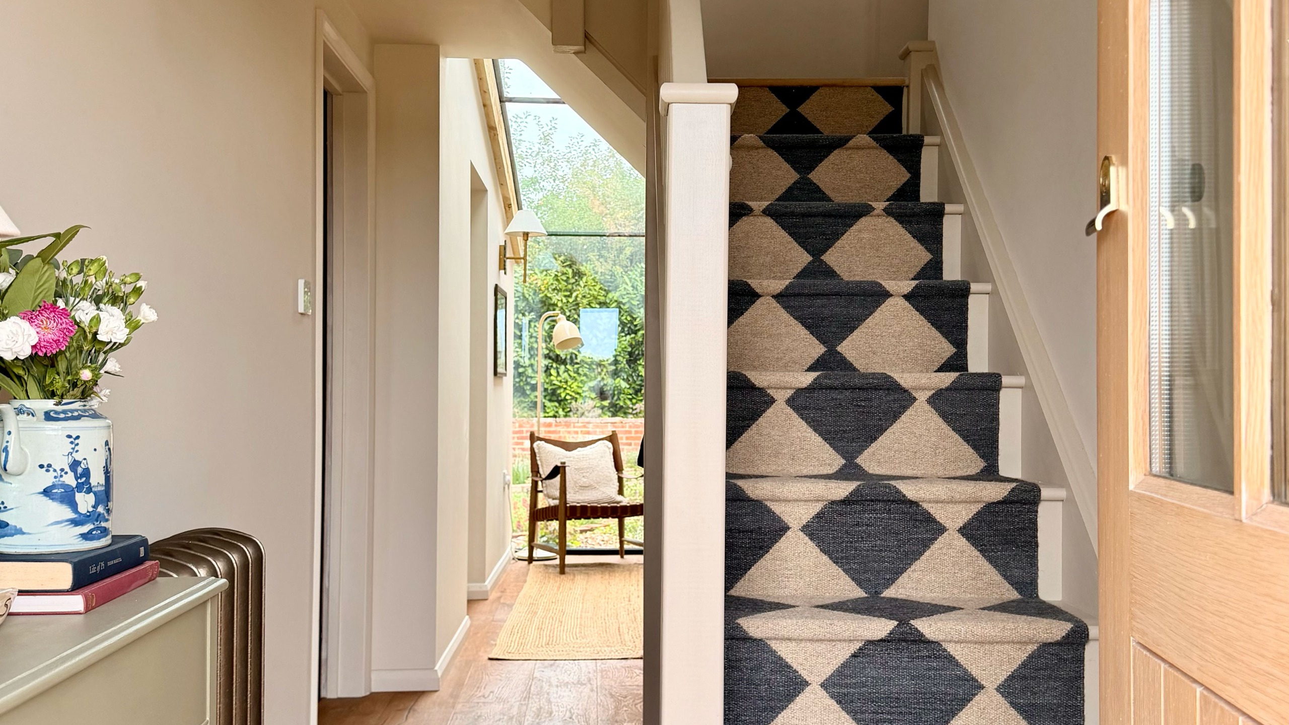 Entrance hall with neutral walls, wooden flooring and monochrome chequered runner up staircase