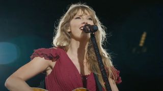 Taylor Swift wearing pink dress singing Our Song during her Eras Tour with a guitar.