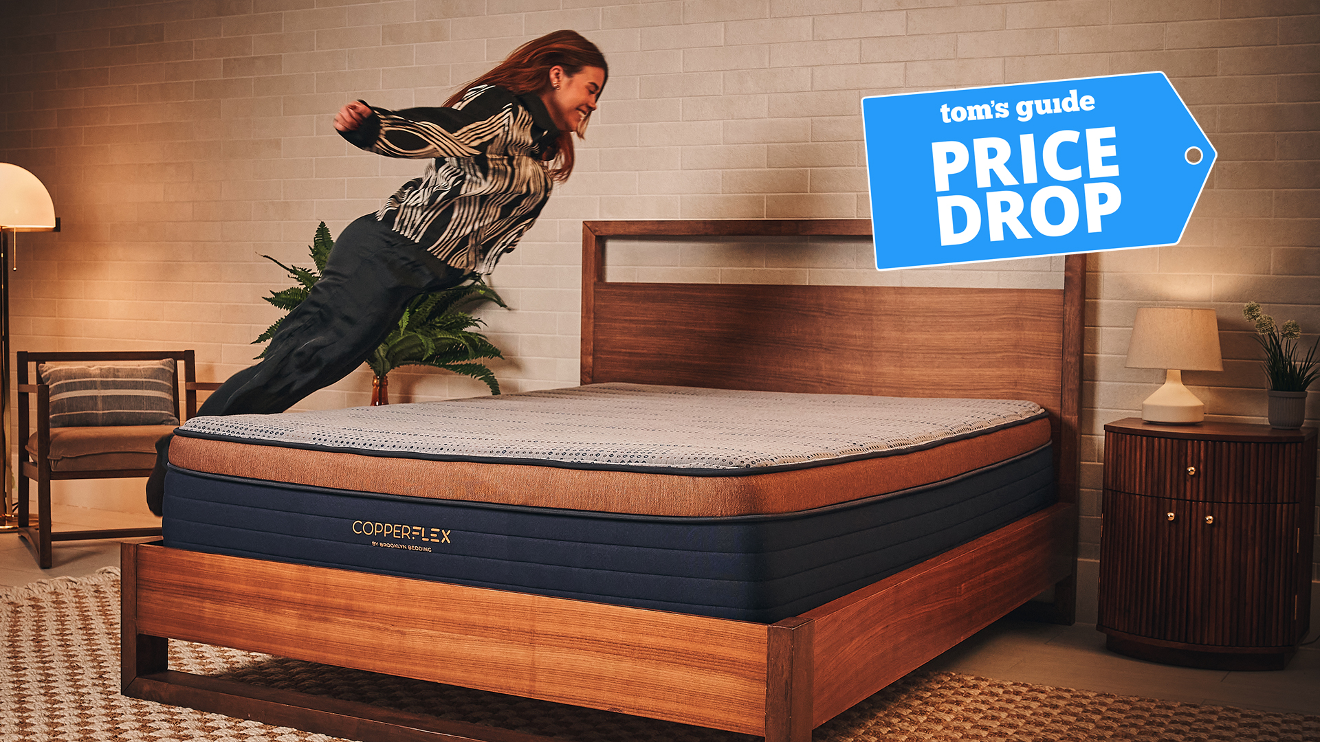 Mattress tester Eve Davies leaps onto the Brooklyn Bedding CopperFlex Pro Mattress in a warmly lit room. In the top right corner is a Tom's Guide price drop deals graphic