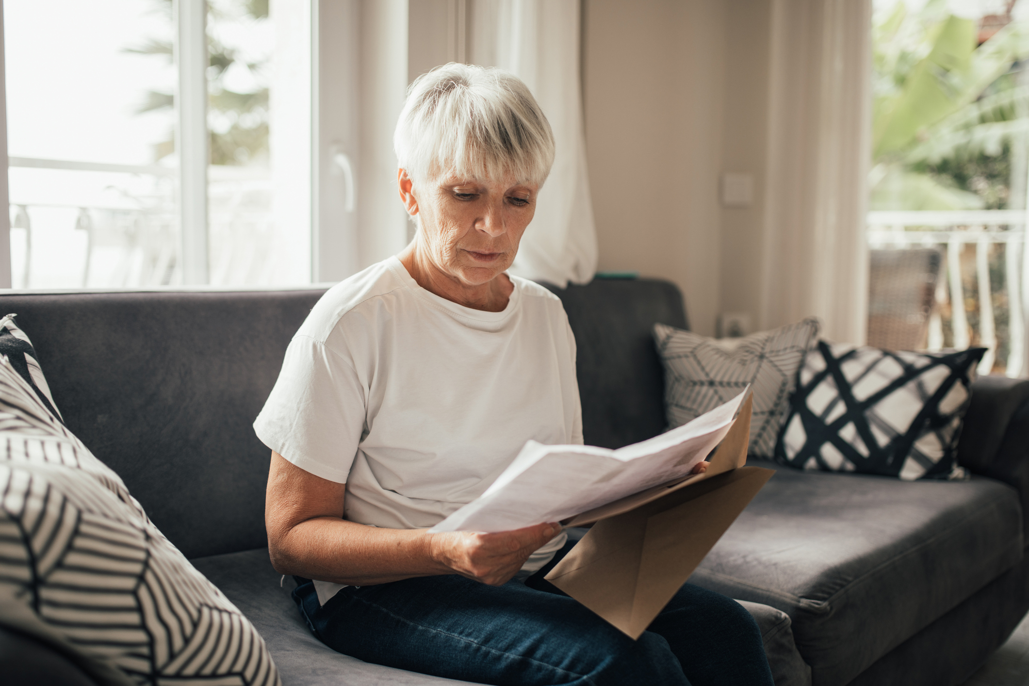 Grey-haired senior woman reviewing paper financial statements and bills at home