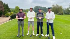 Four golfers holding drivers pose for a photo on a tee
