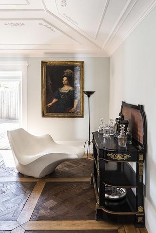 Alternative view of the living area at House of Birds featuring wooden floors, light coloured walls, decorative plaster ceiling, framed wall art, a lamp, a black and gold unit with multiple glass decanters and a white asymmetrical seat