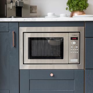Microwave set into a dark grey kitchen unit with a white worktop and a coffee machine on the worktop above