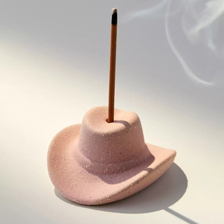 A pastel pink cowboy hat shaped incense holder and stick