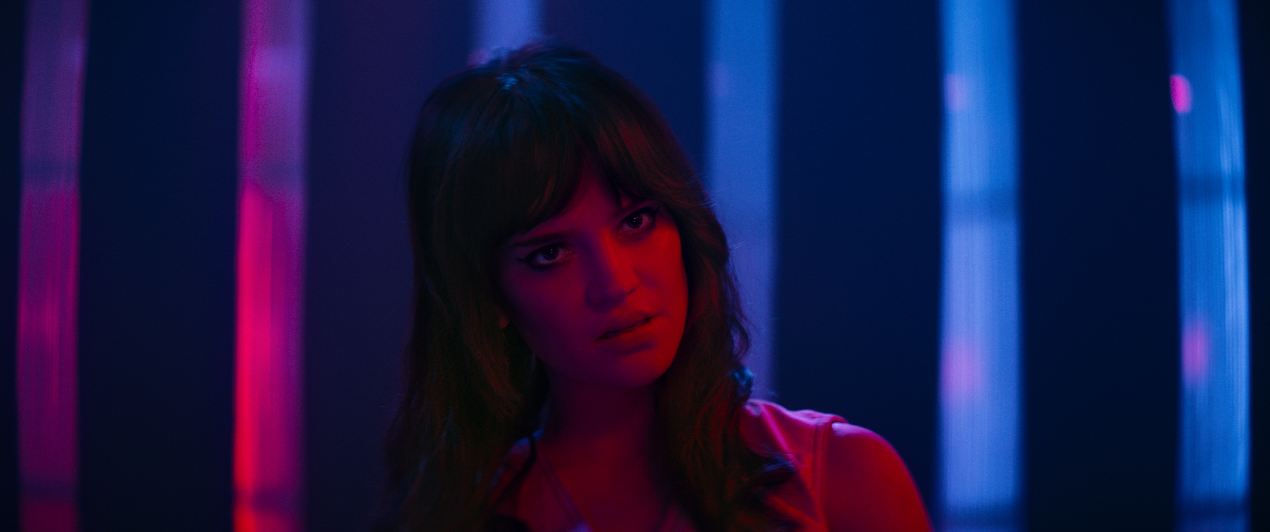 sophie thatcher in a pink and blue lit room looking shocked in a still from the movie her private hell