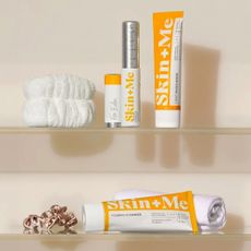 A collection of Skin + Me products placed on glass shelves along with a hair scrunchie, face towel, and head band