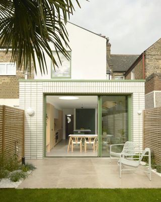 a white tiled extension with green patio doors. Inside you can see a dining table, with a round skylight above