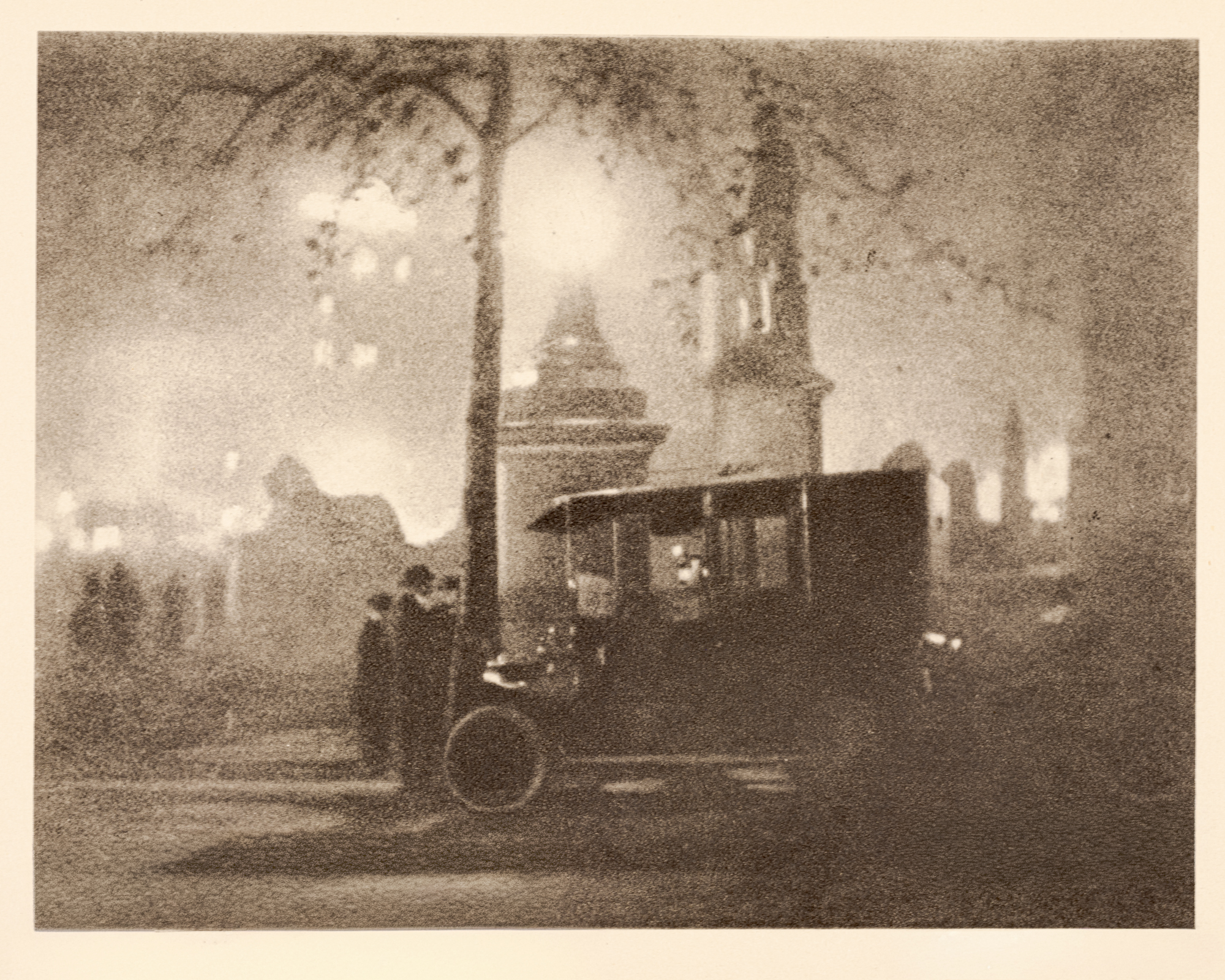 A grainy night scene of an open-topped vehicle parked beneath bare tree branches near a stone monument, with hazy building silhouettes glowing in the background.