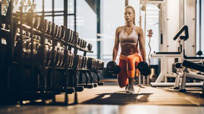 A woman performing a dumbbell lunge as part of a glute workout