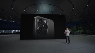 The black titanium Apple iPhone 15 Pro on a screen in a futuristic looking warehouse