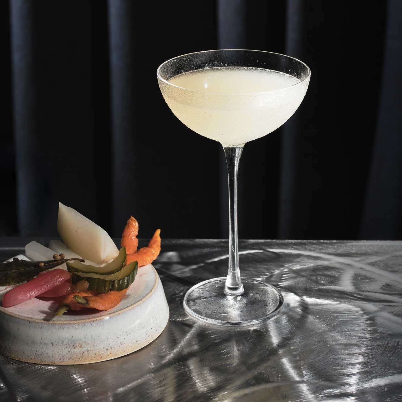 Cocktail on a bar with a plate of pickles