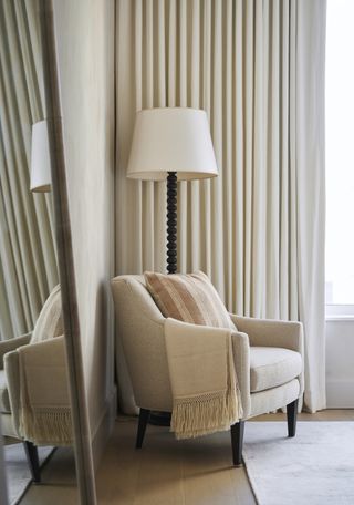 bedroom corner in neutral colors with chair, floor lamp, curtains and mirror