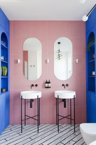A small bathroom with pink wall tiles and blue cabinets