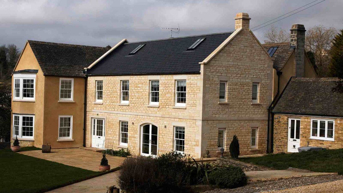 A large Georgian-style detached farmhouse clad in creamy stone and render. The house features a number of windows by the The Sash Window Workshop