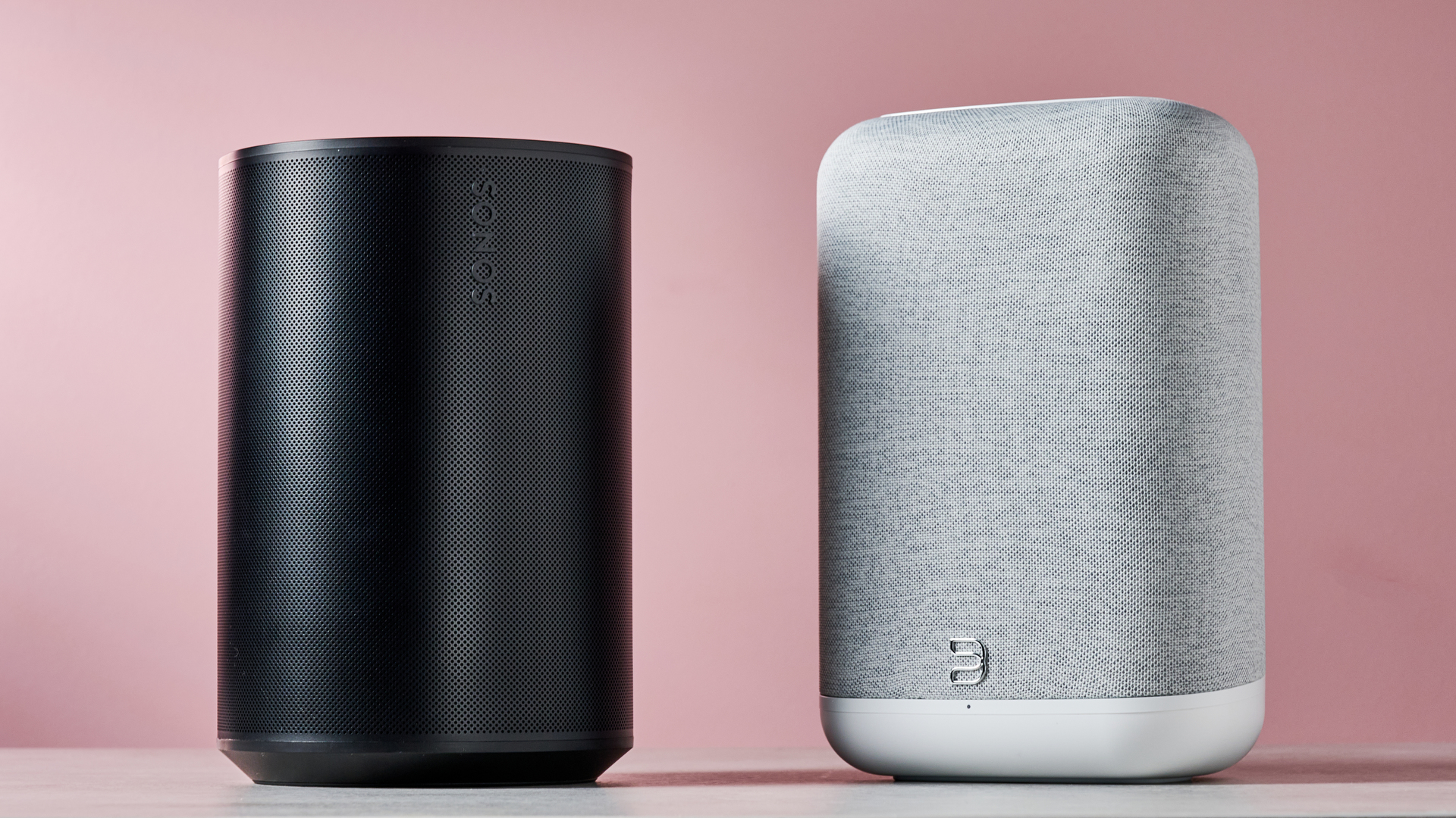The Sonos Era 100 on the left and the Bluesound Pulse Flex on the right in front of a pink background.