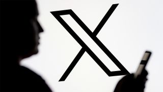 Black and white X logo with blurry person holding a smartphone in the foreground