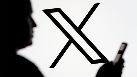 Black and white X logo with blurry person holding a smartphone in the foreground