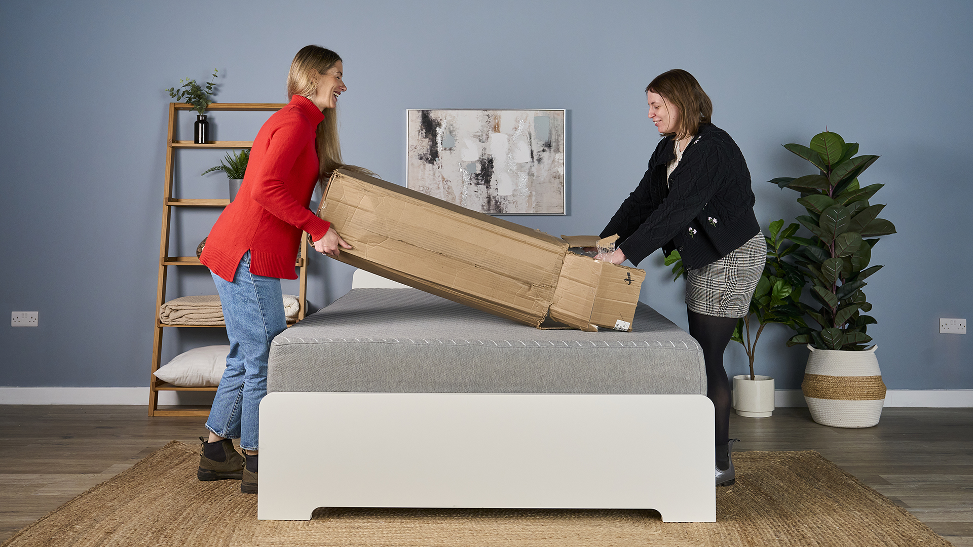 Two of our mattress topper testers position the Helix Dual Comfort Mattress Topper on a bed, ready to begin the unboxing process.
