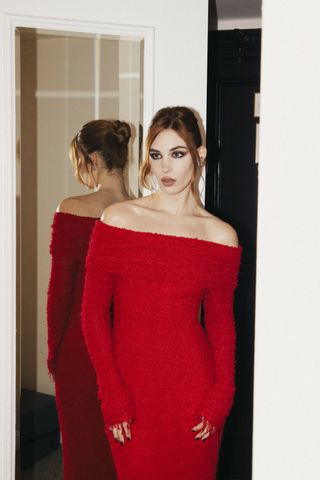 A photo of Nélisse sporting a cherry red bouclé gown with frayed edges and an off-the-shoulder neckline.