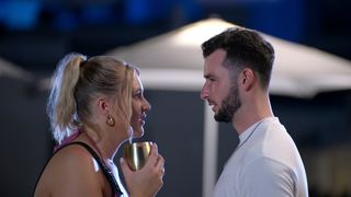 Hannah Jiles (holding a golden wine glass) and Nick Dorka talk while standing in front of a white beach umbrella, in 'Love is Blind' season 7.