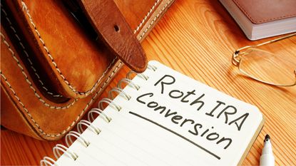 A notebook sits on a desk with the words Roth IRA conversation written on the top page.