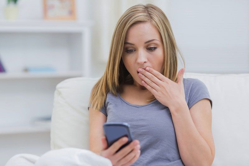 A woman looknig at cellphone with a surprised expression.