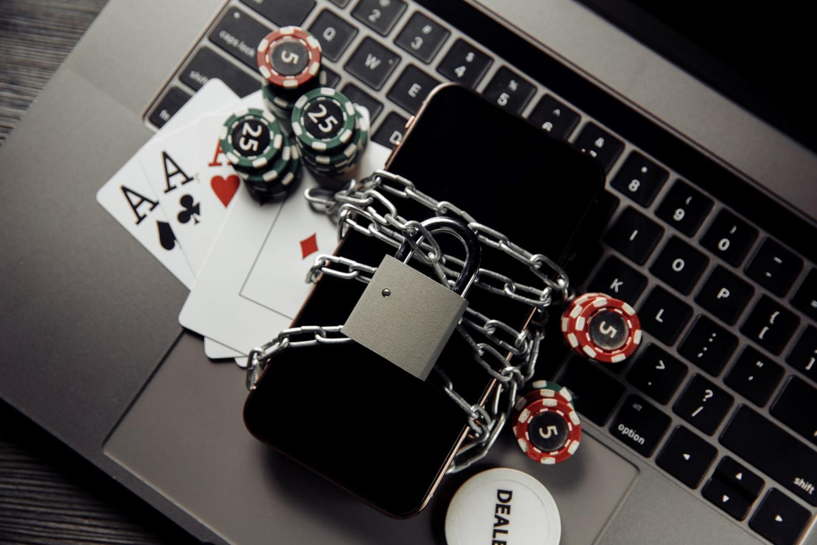 Mit einer Kette verschlossenes Smartphone, das neben Pokerchips und Spielkarten auf einem Laptop liegt.