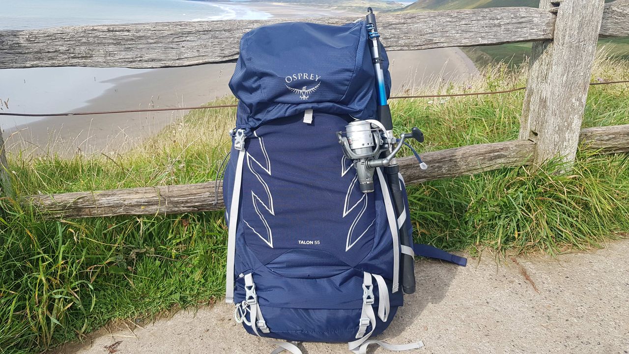Osprey Talon 55 backpack leaning against a fence on a cliff, with a long beach in the background