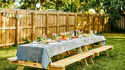 A large wooden bench set with plates for a dinner party with a fence in the background