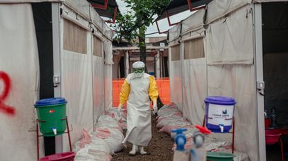A health worker in full protective equipment next to medical supplies
