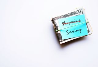 On white copy space, cash dollars money with note written SHOPPING (cross to) SAVING - concept of personal finance goal setting to start saving instead of spending money, for financial security