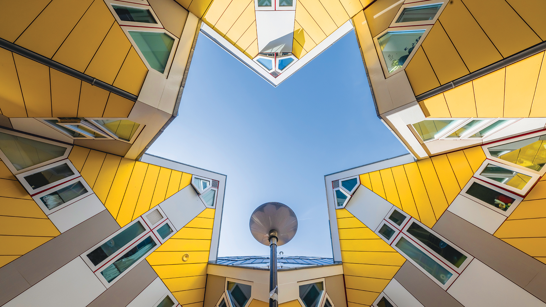 A star-shaped view looking up at modern buildings with yellow façades and colorful windows against a clear blue sky