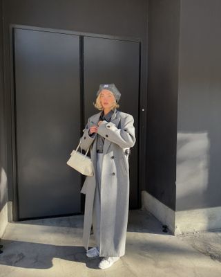 Elsa Hosk wearing a gray Miu Miu beret with a long gray coat, a gray top, gray pants, white sneakers, and a white bag.