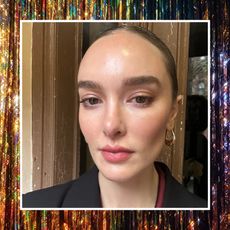 a woman with glitter eyeliner and a black jacket with gold hoop earrings on a sparkle background