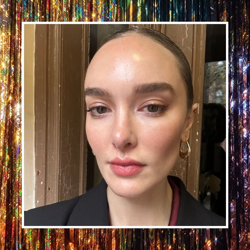 a woman with glitter eyeliner and a black jacket with gold hoop earrings on a sparkle background