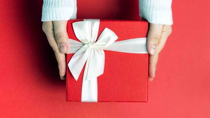 A person holding out a red Christmas present against a red background