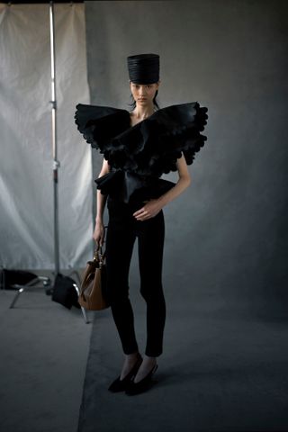 Altuzarra model wearing a cropped black jacket and tan cigarette pants with black flats.