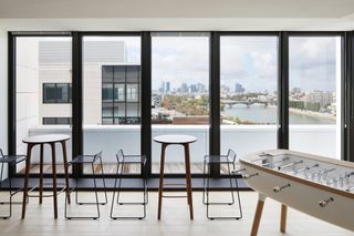 Room with table and chairs, pinball table and view of city and river