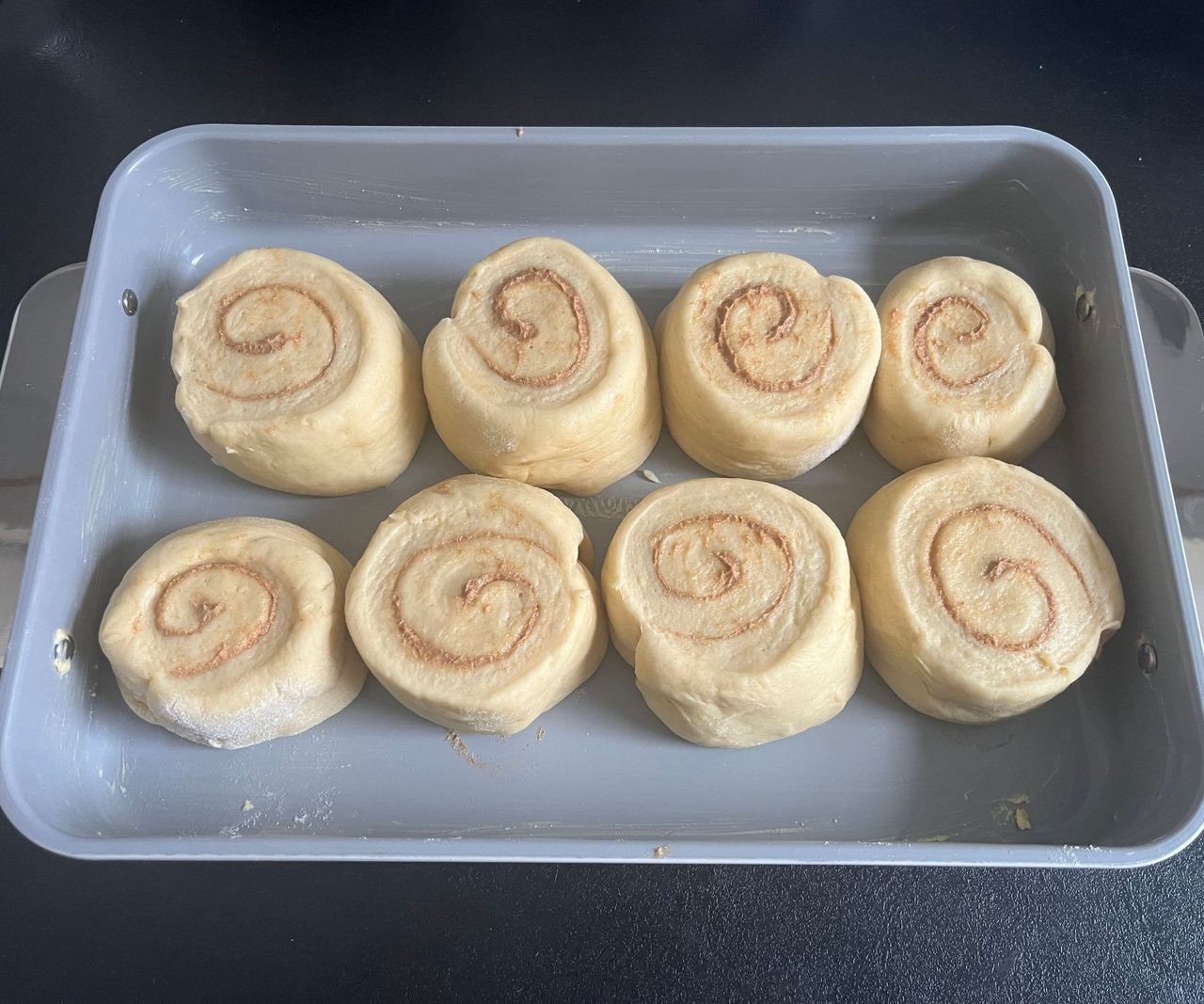A baking tray of unrisen cinnamon rolls on a black counter.