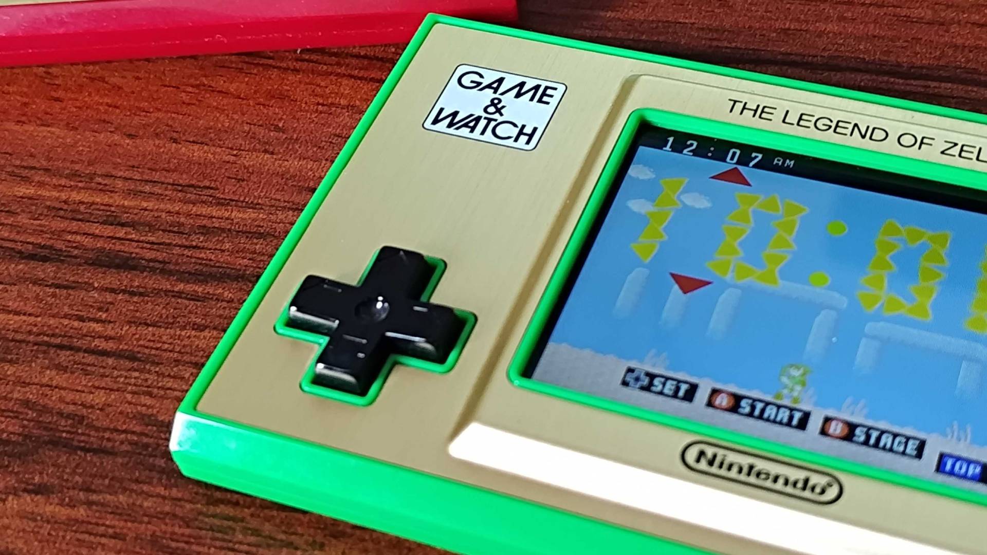 Close-up of Zelda Game & Watch D-pad, screen, and logo with handheld sitting on woodgrain desk.