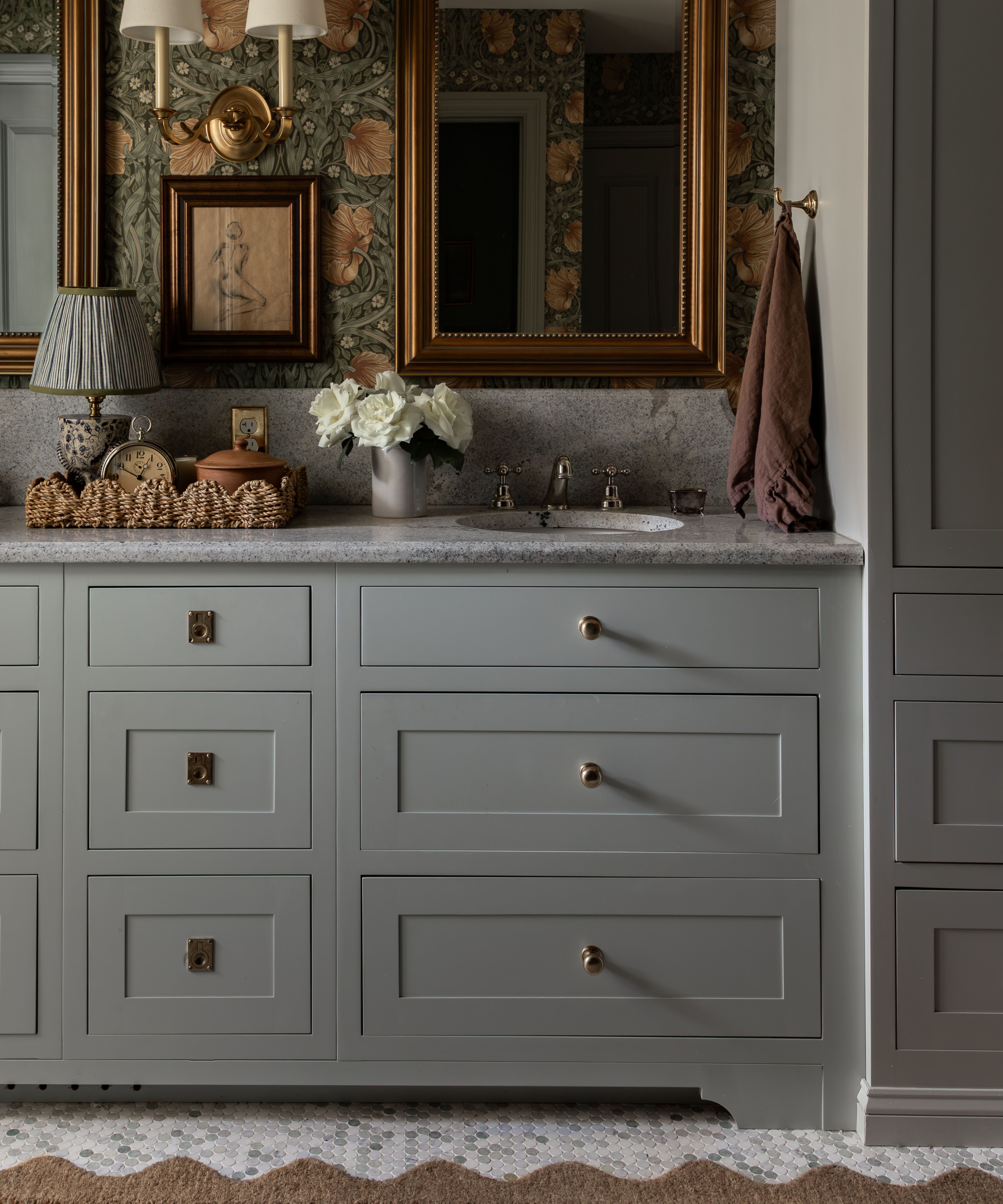 a soft gray blue bathroom with built in cabinetry and sink vanity with marble top, Morris &amp;amp; Co wallpaper, gold mirrors and a scalloped rug