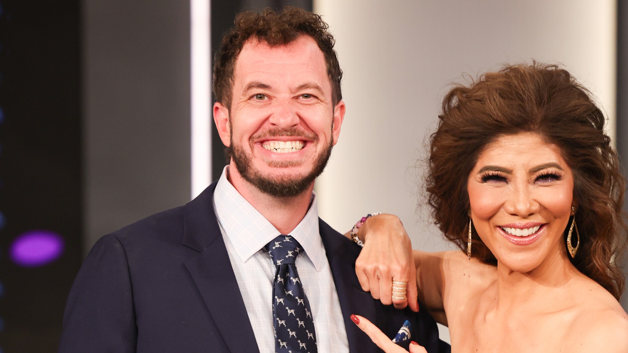 Rick smiling on the Big Brother stage with host Julie Chen Moonves after winning Season 28. He has a suit and tie on and they're both smiling,