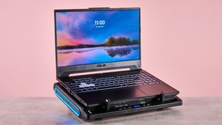 The Llano V10 Gaming Laptop Cooling Pad at a 3/4s angle with an open ASUS gaming laptop on top of it in front of a pink background.