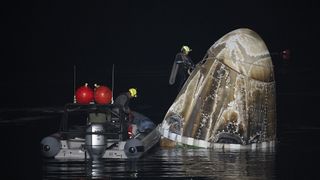 A SpaceX Crew-7 Dragon capsule bobs in the ocean as recovery teams work to secure it at night.
