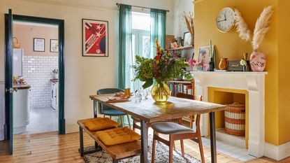 dining room with a mustard yellow feature wall, industrial style dining set and a large vase of flowers