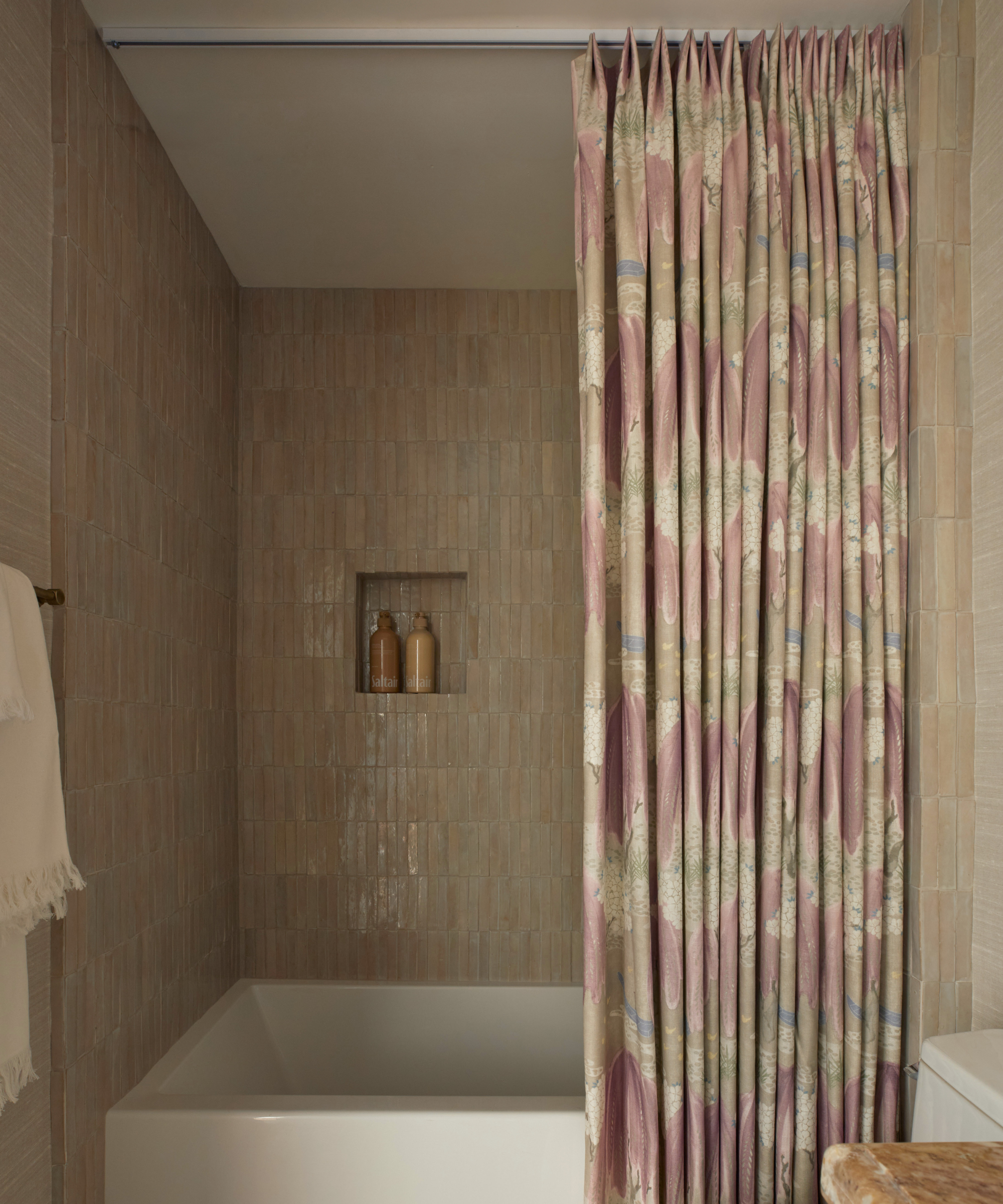 a bathroom with soft pink tiled walls, a white built-in tub, and a pink shower curtain mounted to the ceiling