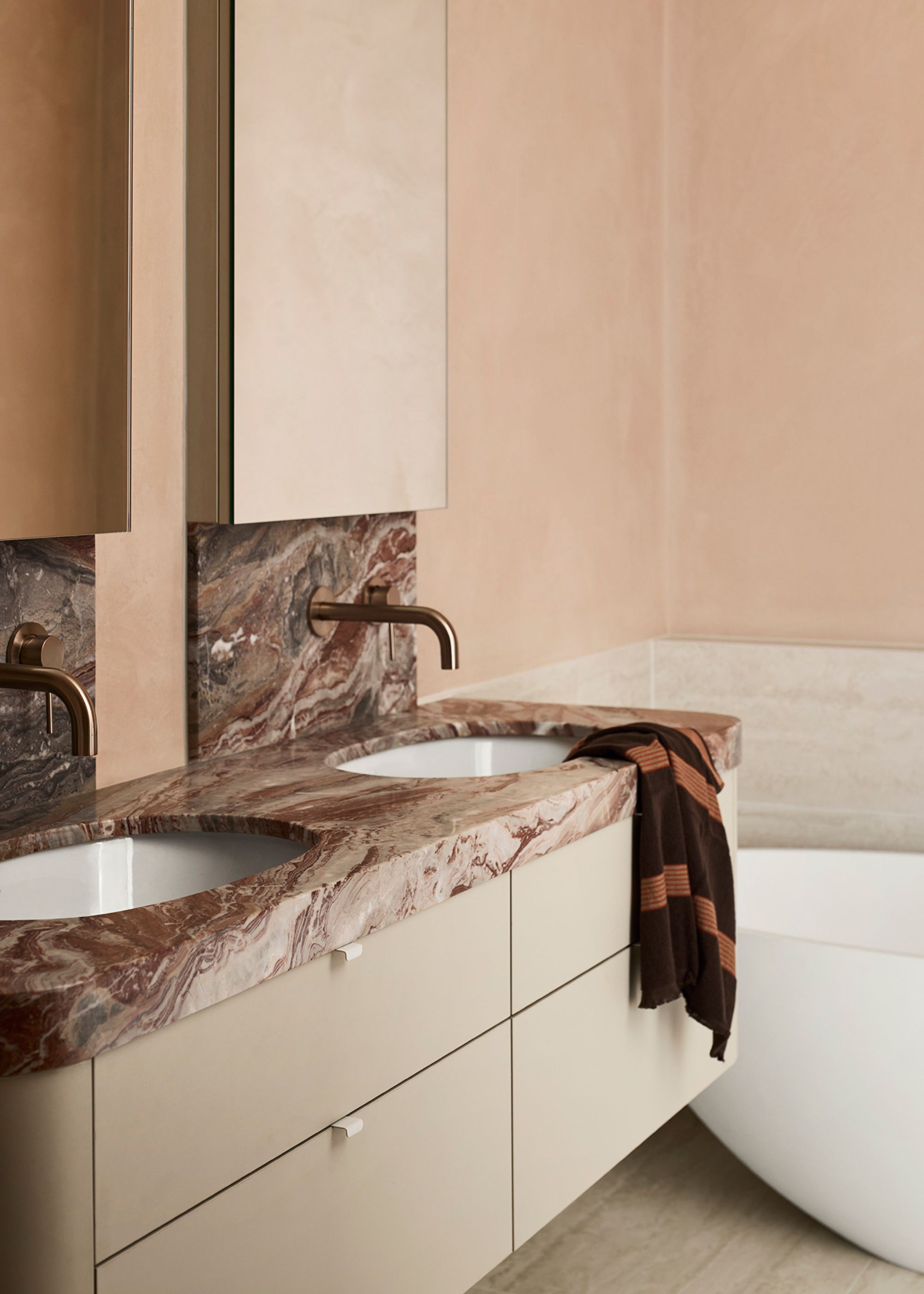 A bathroom with mirrored cabinets, a floating sink, a marble backsplash, a striped towel, and beige drawers