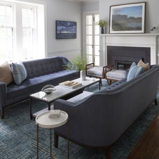 blue and white living room with matching blue sofas, marble topped coffee table, stools, side table, artwork, textured rug