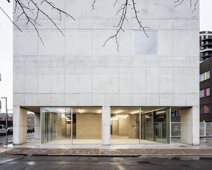 Street view of grey building with minimal windows and glass doors on bottom level.