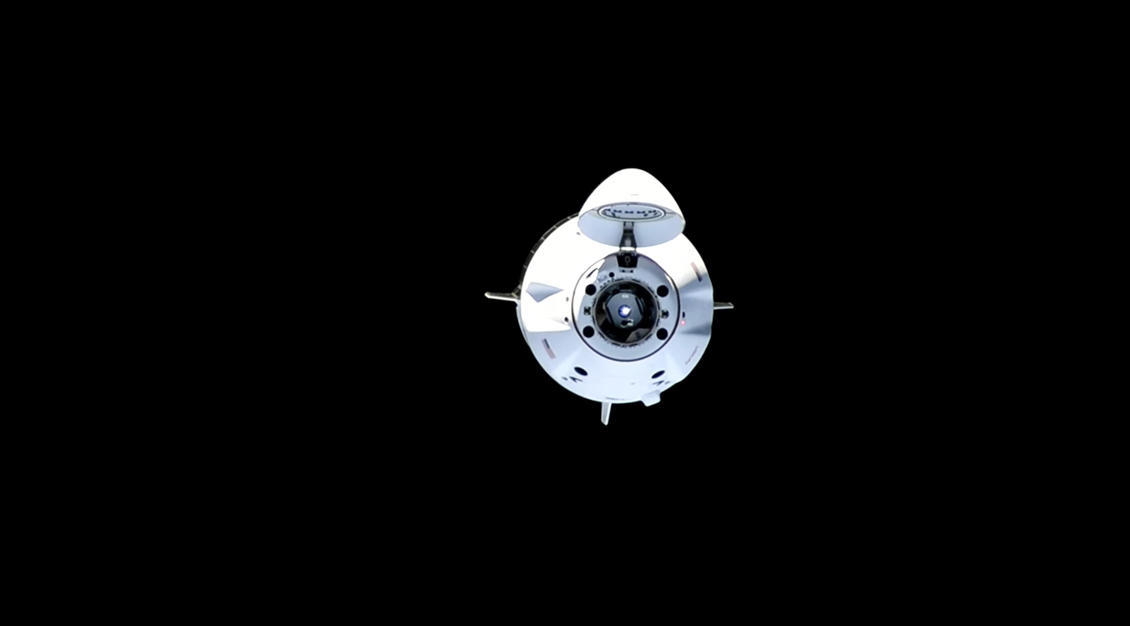 crew dragon in the middle distance during docking with international space station with black space behind